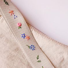 a close up of a ribbon on a white surface with flowers and leaves embroidered on it