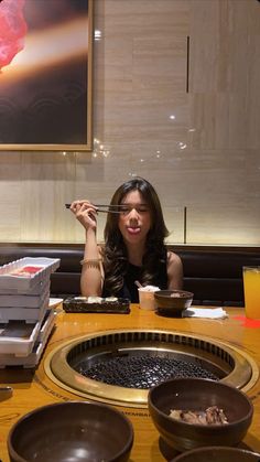 a woman sitting at a table eating sushi with chopsticks in front of her