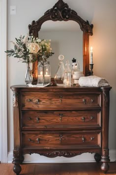 an antique dresser with candles and flowers on top is shown in front of a mirror