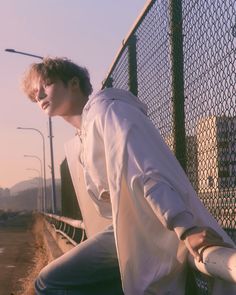 a young man leaning against a fence with his hands on the rail and looking off into the distance