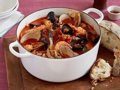 a large pot filled with seafood next to bread on a wooden cutting board and pink table cloth