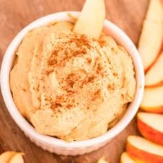 an apple and cinnamon dip in a white bowl surrounded by sliced apples on a wooden table