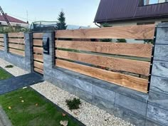 a wooden fence in front of a house with grass and rocks on the ground next to it