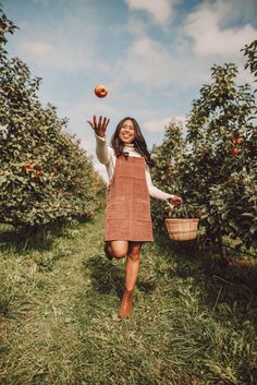 a girl in an apple orchard throwing an orange into the air with her hands and smiling