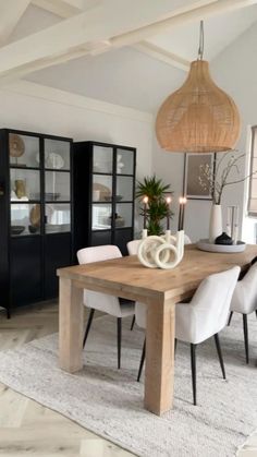 a dining room table with white chairs and a vase on top of it, in front of a black cabinet