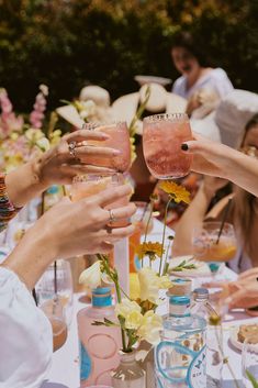 people are toasting at a table with drinks and flowers in vases on it