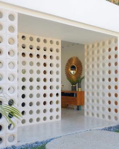 an entrance to a house with white walls and round holes on the wall, in front of a potted plant