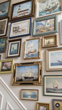 a wall full of pictures and paintings on the side of a stair case in a house