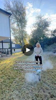 a woman standing on top of a grass covered field next to a yard with a lawn mower