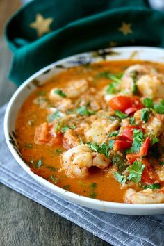 a white bowl filled with shrimp and tomato soup on top of a green cloth next to a napkin