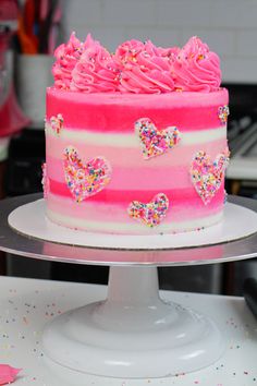 a cake with pink frosting and hearts on it sitting on top of a table