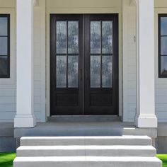 two black double doors sitting on top of a set of steps next to a white house