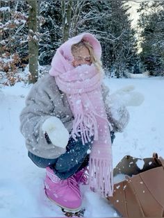 a woman kneeling down in the snow with a pink scarf around her neck and boots on