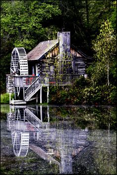 an old water mill sits on the edge of a lake with trees in the background