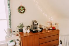 a coffee maker on top of a wooden cabinet in a room with christmas decorations and lights