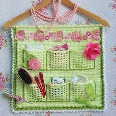 a green crocheted purse with pink flowers and beads hanging on a wall next to a wooden hanger