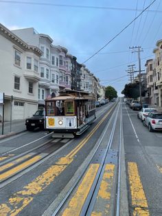 a trolley car is traveling down the street in front of some buildings and parked cars