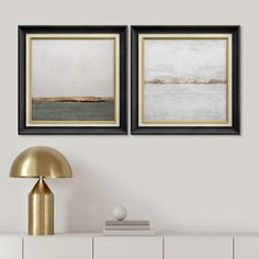 two framed art prints on a wall above a white dresser with a gold lamp and side table