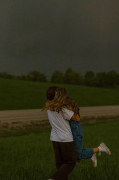 two people are hugging in the middle of a field under a dark sky with storm clouds