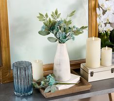 a vase with flowers and candles on a table in front of a mirror next to other items