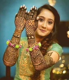 a woman holding her hands up to show the henna designs on her hand and arm