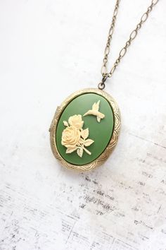 This is a gorgeous statement necklace with a big oval locket pendant in antique brass. The focal on the front of the locket is a resin cameo with an ivory cream humming bird and flower on a green background. This photo locket has beautiful details and will be a lovely accessory to store your treasured photos and mementos. This would be a beautiful gift for mom or anyone that loves romantic nature inspired accessories.  Details:  ~ The locket measures 1.5"w x 1.75 "h (36mm x 45mm) and has two ova Secret Hiding Spots, Nature Inspired Accessories, Romantic Nature, Hummingbird Necklace, Bird And Flower, Oval Locket, Humming Bird, Frame Photo, Floral Photo