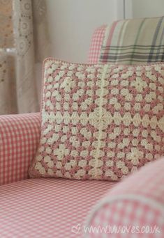 a pink and white checkered couch with pillows on it's back, in front of a window