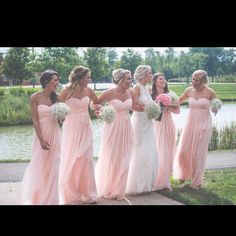 a group of bridesmaids standing next to each other in front of a lake