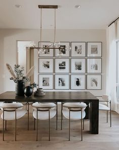 a dining room table with white chairs and pictures on the wall behind it, all in black and white