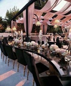 a long table with black chairs is set up for an outdoor wedding reception in the evening