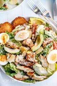 a salad with chicken, hard boiled eggs and lettuce in it on a white plate