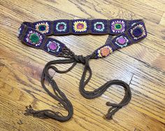 a purple crocheted belt with flowers on it sitting on a wooden floor next to a pair of scissors