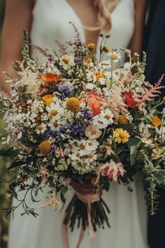 a bride and groom standing next to each other holding a bouquet of wildflowers