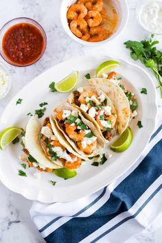 shrimp tacos on a white plate with limes and salsa