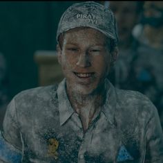 a man wearing a hat and smiling in front of other men with snow all over his face