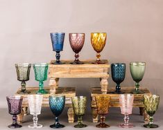 many different colored glass goblets sitting on a wooden table with one standing in the middle