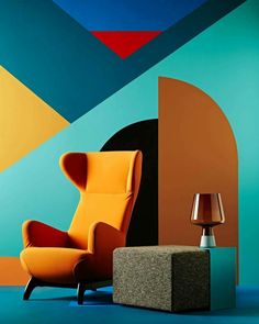 an orange chair sitting next to a lamp on a blue floor in front of a colorful wall