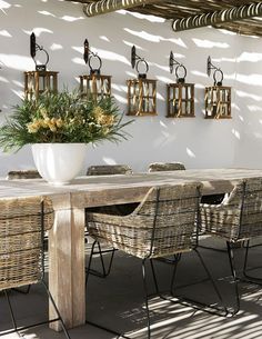 an outdoor dining table with chairs and potted plants on it in front of a white wall