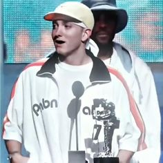 a male in a white shirt and black hat is holding a silver trophy while standing next to another man