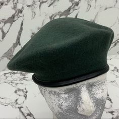 a green hat sitting on top of a mannequin's head in front of a marble wall