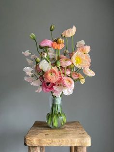 a vase filled with pink and white flowers on top of a wooden table next to a gray wall