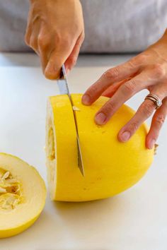 a person cutting into a piece of cheese on top of a white counter with a knife