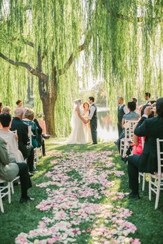 a bride and groom standing under a willow tree during their wedding ceremony at the park