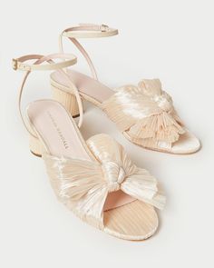 Pleated mid-heel sandal in cream fabric topped with our signature knotted bow. Features a padded footbed with gold stamped logo. Open toe with adjustable buckle ankle strap. 2 inch heel. Feminine Cream Low Heel Sandals, Feminine Cream Block Heel Sandals, Elegant Cream Sandals With Buckle Closure, Cream Sandals With Buckle Closure For Evening, Feminine Cream Ankle Strap Sandals, Elegant Cream Sandals With Wrapped Heel, Luxury Cream Sandals With Block Heel, Luxury Cream Block Heel Sandals, Loeffler Randall Shoes