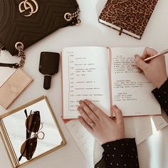 a person is writing in a notebook on a table with other items and accessories around them