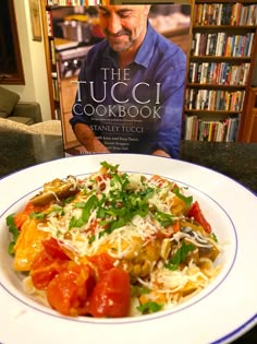 the cookbook is next to a plate of food on a table with a bookcase in the background