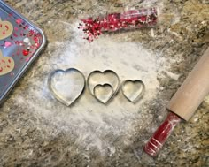 three heart shaped cookie cutters sitting on top of a counter next to a rolling pin