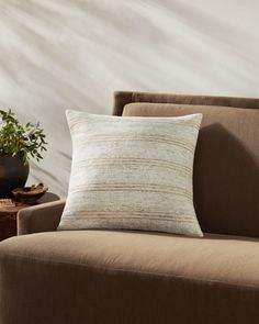 a brown couch with a white pillow on top of it next to a potted plant