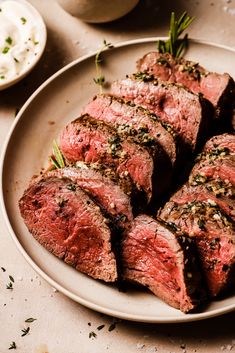 a white plate topped with sliced up steak on top of a table next to bowls and utensils