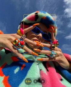 a woman with colorful nails and sunglasses holding up her hand in front of the camera